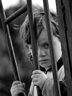sad, angry boy behind iron fence